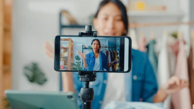 A woman holds a smartphone displaying a video call, engaging in short-form video content.
